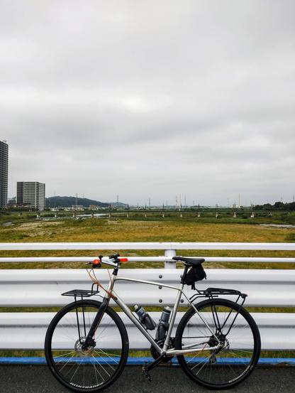 A silver flat bar bike on a Tokyo road bridge on the Tama River looking towards the Okutama mountains. The sky is grey.