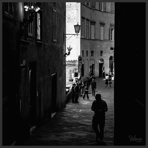 Shady street. A man in a hat strolls through the streets of Siena. Tuscany, Italy. Black and white photography. Copyright Silvijo Selman.