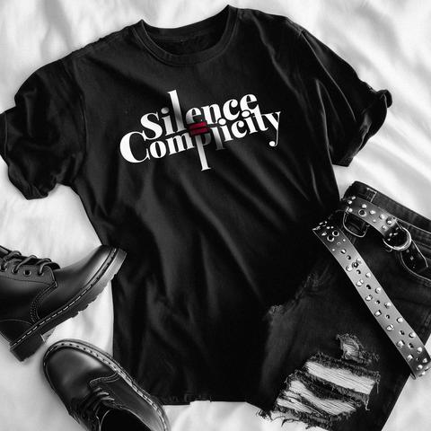 Schwarzes T-Shirt mit dem weißen Slogan „Silence is Complicity“ in Serfifenschrift. Das Wort „is“ ist durch ein rotes "ist-gleich-Zeichen" ersetzt, das mittig zwischen den beiden Worten steht und wodurch der Satz grafisch betont wird. Das Design steht für Zivilcourage und die Botschaft, dass Schweigen gegenüber Ungerechtigkeit Mitschuld bedeutet.
