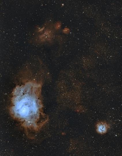 This image is a photograph of the Lagoon and Trifid Nebulae, which have been processed using the Foraxx Palette. As a result, the celestial bodies are golden, blue, and a rosy shade of orange. 