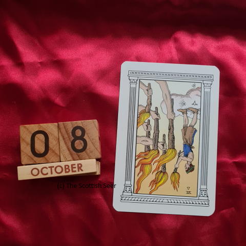 A photo of a wooden block calendar showing the date 08 October next to a tarot card - the 6 of wands reversed. The card shows a man standing on a cloud holding a flaming stick (wand) in front of him. There are 5 outstretched hands with flaming sticks being held in front of him by unseen people.