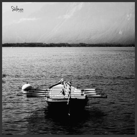 Serene Reflections. A floating wooden rowboat on the tranquil waters of Lake Geneva. Montreux, Switzerland. Black and white photography. Copyright by Silvijo Selman.