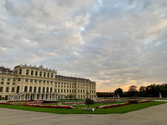 Flower garden in front of a yellow castle. Cloudy sky with an orange glow.