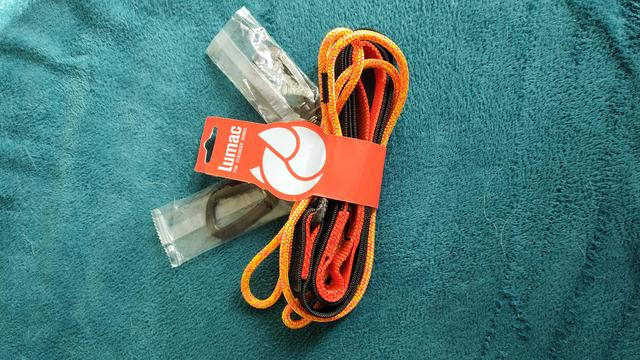 Eine orange-farbene Leine, noch verpackt, und zwei ebenfalls verpackte schwarze Karabiner liegen auf einer petrol-farbenen Decke.