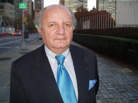 Man looking towards camera with gray hair wearing a suit and blue tie. 