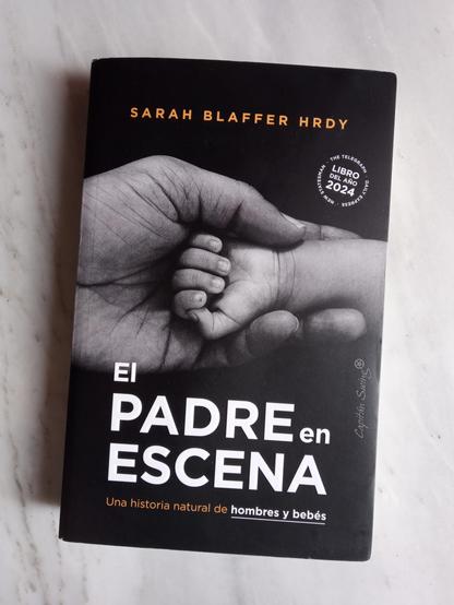 El padre en escena. Una historia natural de hombres y bebés, de Sarah Blaffer Hrdy, publicado por Capitán Swing y traducido por Patricia Teixidor. La cubierta, de fondo negro, muestra una mano adulta sosteniendo el antebrazo de una criatura. La imagen es en blanco y negro.