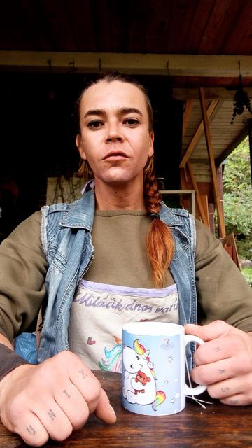 A photo of a person sitting in front of camera and holding a coffee mug.  Waist up.
