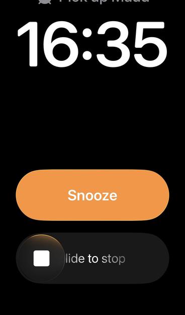 A screenshot of the alarm screen in iOS 26.1b2. There are two controls: a Snooze button and a “slide to stop” bar. On the iPhone mini, the text on “slide to stop” is cut off, only showing “lide to stop”