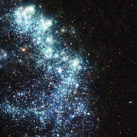 An arc of blue points makes a rough backwards C shape on the black background of space. These points are hot, young stars or star clusters. Interspersed within the blue points are red points, which are cooler stars. Near the edges of the arc are hazy areas of nebulosity.