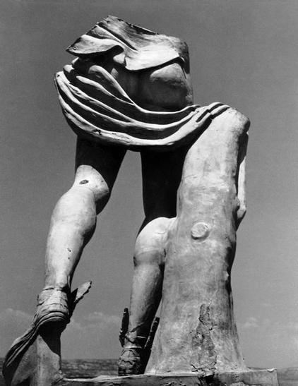 Marble sculpture of Hermes atop a roof. His upper body is missing but he can be identified by his winged sandals. A himation is draped around him but it goes underneath his bottom, letting us peek at his shapely buttocks.
