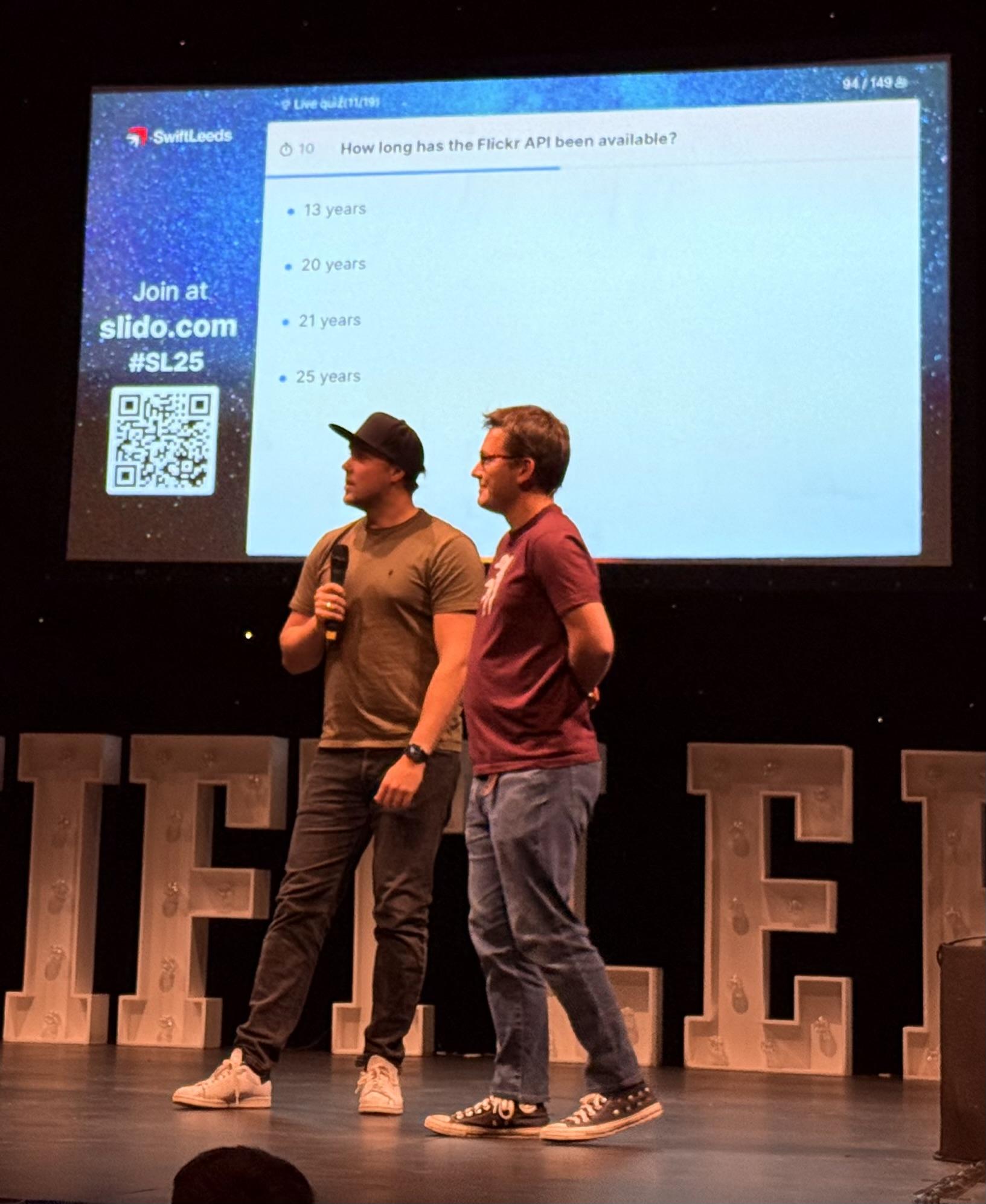 Two hosts of the game show at the end of Swift Leeds 25, discussing the question of how long Flickr’s api had existed.