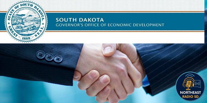 Handshake with suited arms in focus, featuring the South Dakota Governor's Office of Economic Development text and state seal, calm mood.