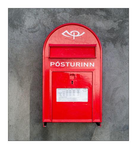 Roter isländischer Briefkasten auf grauer Betonwand. Aufschrift "Posturinn".