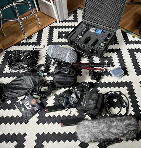 Farbfoto von Tonaufnahme Equipment welches wild auf einem schwarz weißen Teppich ausgebreitet liegt. 