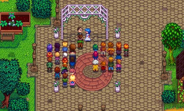 a screenshot of the video game star dew valley showing an aerial view of the villagers standing in rows , faving a large pink lattice arch .
under the arch stand sid dressed in a black suit , and emily in a white wedding dress .
green grass and trees frame the picture