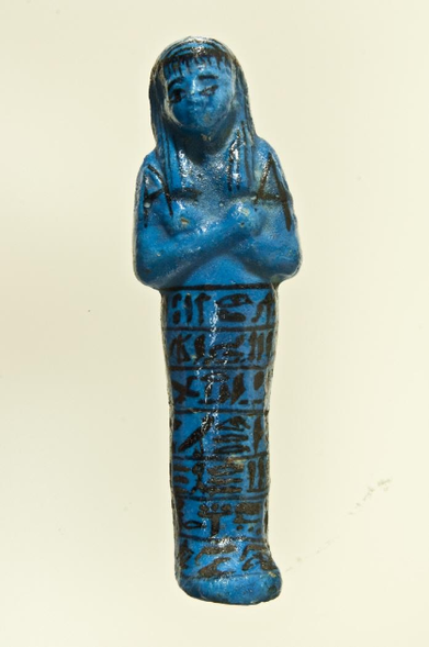 Figura azul con los pies unidos y los brazos cruzados. Tiene jeroglíficos pintados de cintura para abajo.