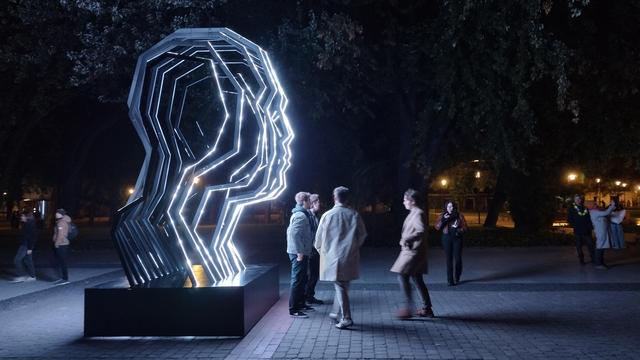 Light Move Festival 2025 in Łódź - The Kinetic Art of Light Festival: people in front of color-changing light sculpture in the form of a human face silhouette.