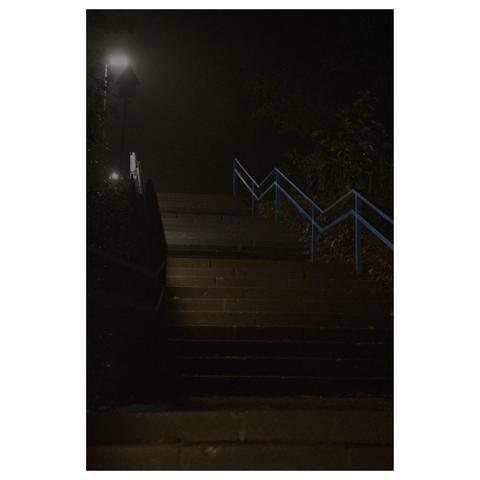 Nacht-Fotografie. Eine lange Treppe mit blauem Geländer erstreckt sich einen Hang hinauf. Der Betrachter schaut die Treppe hinauf. Eine einsame Straßenlaterne steht am Ende der Treppe vor schwarzem Himmel und setzt einen zaghaften Lichtpunkt. 