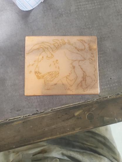 Plaque de cuivre, dessin au trait d'un chien à toutes petites dents, gueule ouverte et pleurnichant, les pattes rentrées sous lui et des cornes bizarres lui sortant de la colonne vertébrale