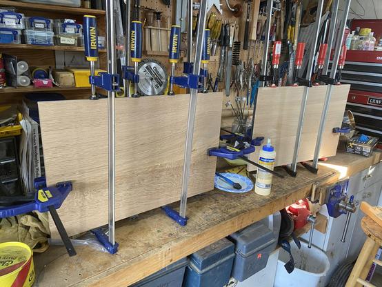 Two wood shelves in the clamps for a glue up.  Woodworking clamp p0rn!  The shelves sit on a busy workbench with tools above and tool boxes below.
