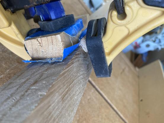 Not so great pix of a dutchman patch clamped into a notch in a shelf leg.  The black pad on the yellow clamp hids most of the patch.  A blue clamp with a black pad holds a block of wood wrapped in blue tap.  The block helps keep the dutchman in position during clamping.