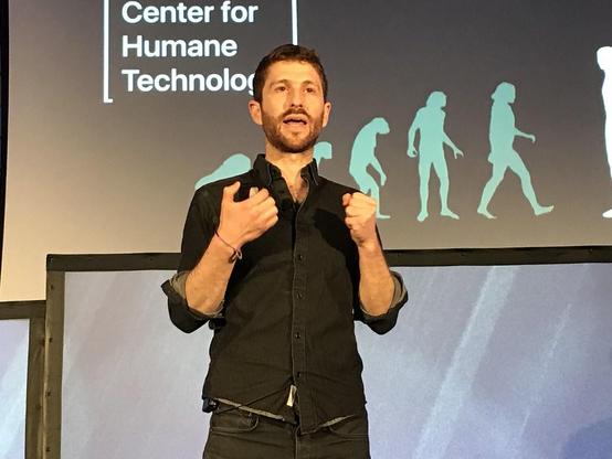 Ein Foto von Tristan Harris bei einem Vortrag
Hinter ihm eine dunkle Leinwand
Mit Clip Art der Mensch in seiner Entwicklung, vom Affen zum Menschen
Dann auch zu lesen
Center for Humane Technology
Er ist Mitbegründer der Center for Humane Technology

Foto nicht meins