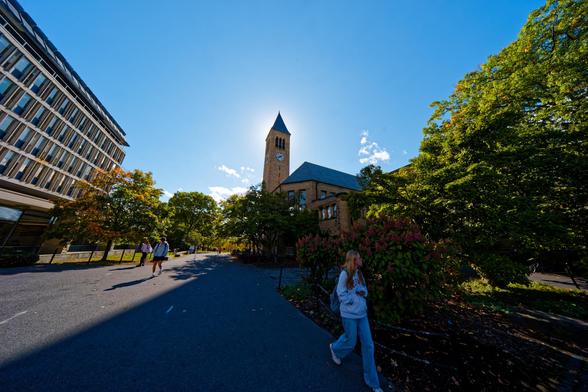 On the left side a concrete building cut like a punched card seems to lean into the frame whie towards the center stands a clocktower obscuring the sun with shadows radiating outward,  such as the one that de-emphasizes the closer people in the frame
