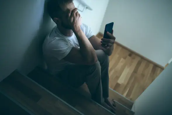 Ein Mann auf einer Treppe, in seiner linken Hand ein Handy, die rechte ist in Verzweiflung über seine Augen gelegt
Wir blicken auf ihn herab

Bild nicht meins