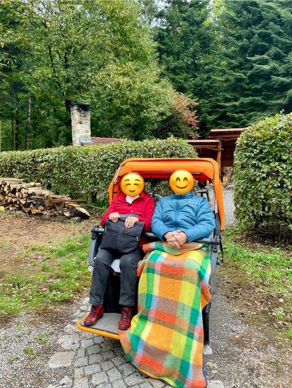Die Rikscha Luise steht besetzt mit zwei glücklichen PassagierInnen auf einem Weg vor einer Hecke.