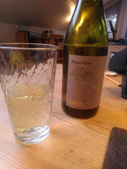 Eine Flasche alkoholfreien Weßwein auf einem Holztisch, daneben ein Apfelweinglas, weil wir sonst keines haben :)