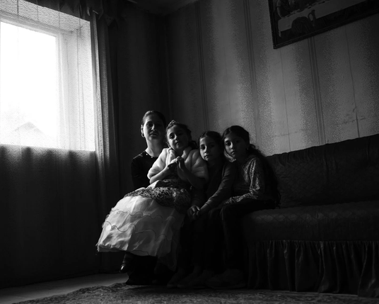 Black and white image of a woman sitting next to three younger girls on a couch looking towards the camera