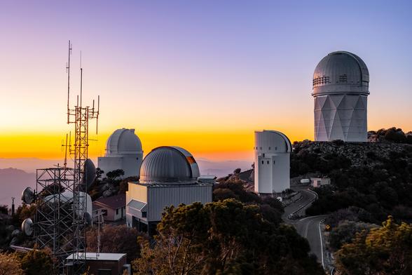 The sun sets at NSF Kitt Peak National Observatory behind the domes of the NSF Nicholas U. Mayall 4-meter Telescope, UArizona 0.9-meter Spacewatch Telescope, UArizona 1.8-meter Spacewatch Telescope, UArizona Bok 2.3-meter Telescope, and UArizona SuperLotis Telescope.
