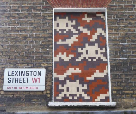 Brown, fawn and grey Invader mosaic in bricked up window. Sign for Lexington Street to the left. Day.