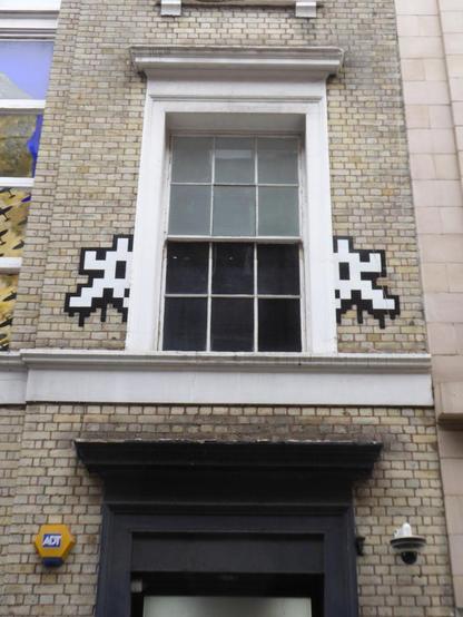 Two halves of white space invader on either side of a tall window on brick building.