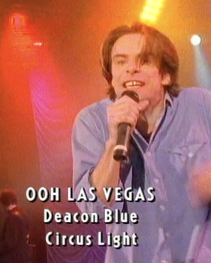 A floppy-haired gap-toothed man with a mic