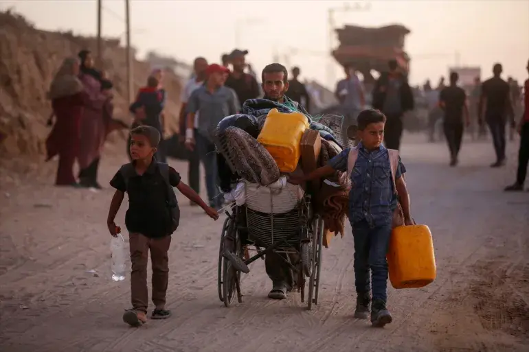 A man with two children pushes a wheelchair with belongings, including orange water container.