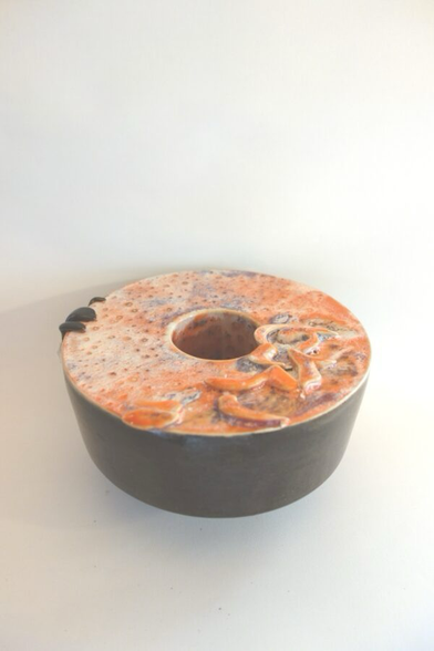 Objekt aus Keramik, Form: wie eine Torte mit kreisrunder Vertiefung in der Mitte, dunkelbrauner Rand, oben mit aufgesetzten Ornamenten, Farben: orange, weiß, blau ineinander verlaufend