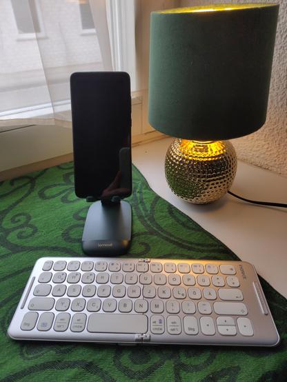 Smartphone auf einem Ständer damit es aufgerichtet stehen bleibt, davor eine silberne faltbare Tastatur