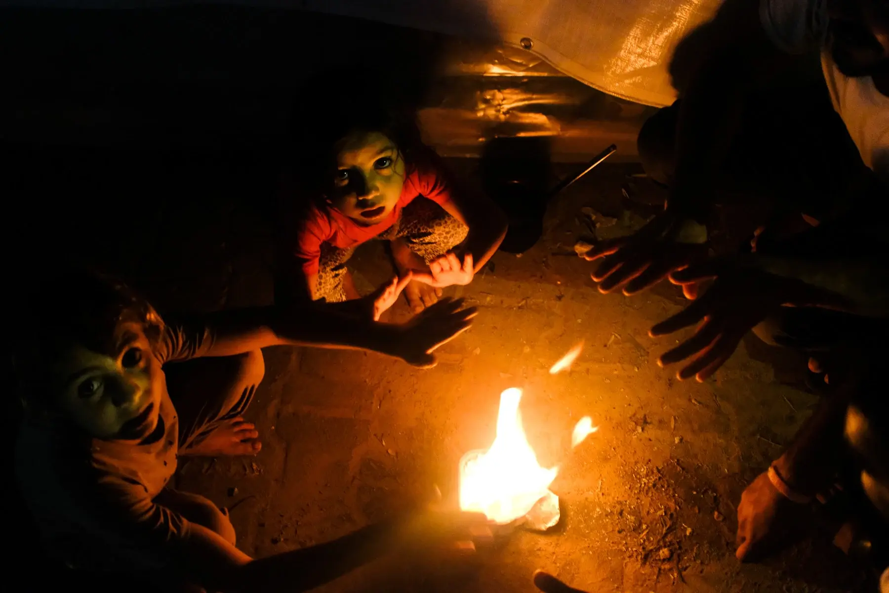 A father and his children warm their hands over a fire.