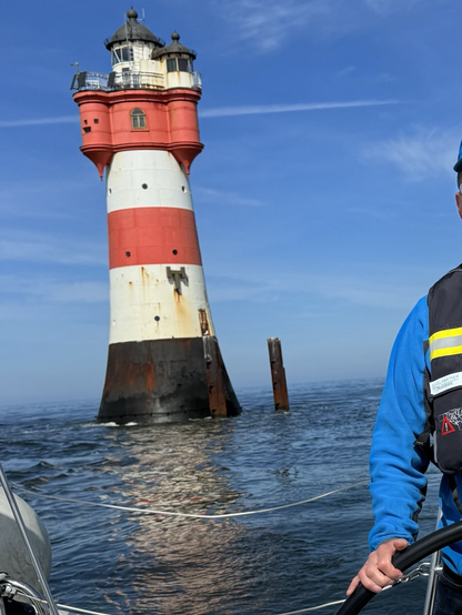 Der ehemalige Leuchtturm Roter Sand von einer vorbeifahrenden Segelyacht aus gesehen. Der rot-weiß gestreifte Anstrich des Turms weist ebenso deutliche Rostspuren auf, wie dessen dunkles Fundament. 