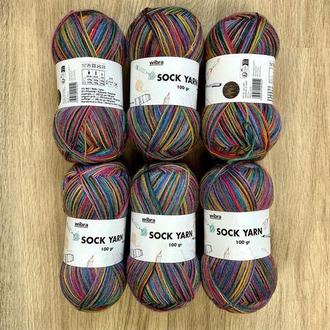 Six balls of very colorful variegated sock yarn on a light wooden background.