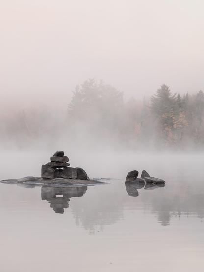 A rocky island in a foggy lake, with stones stacked artistically and soft autumn colors behind.