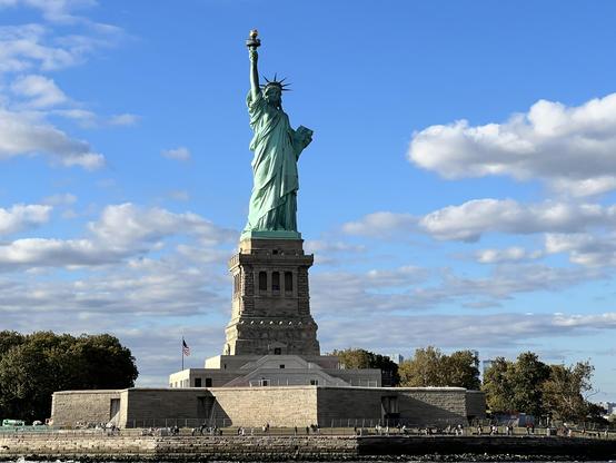 Photograph by Feniochel: The Statue of Liberty, close-up, with pedestal, blue skies and puffy white clouds overhead. 