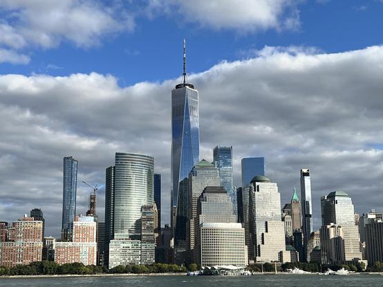 Photograph by Fenichel:
A view of the Southern tip of New York (Manhattan), with the Freedom Tower and surrounding skyline - a dramatic new skyscape since 9/11. Framed by water at bottom and bright blue sky with puffy clouds on top.