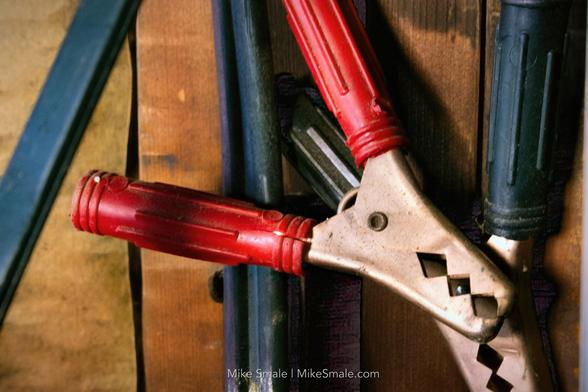 A close-up shot of jumper cables with red and black grips resting against a wooden background.