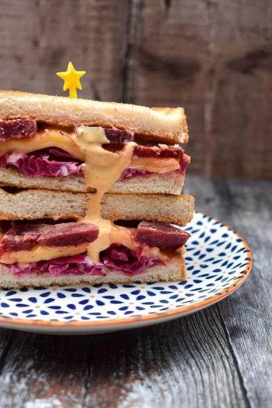 Toasted beet reuben sandwich with russian dressing dripping down the side on a plate.