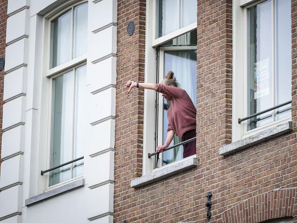 Beeld: ANP
Een omwonende laat duidelijk zien wat ze van de betoging vindt.
Op de foto een vrouw die vanuit haar geopende raam haar arm naar buiten steekt, met een handgebaar waarbij ze haar duim naar beneden houdt.