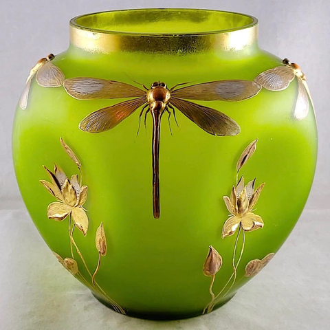 Eine runde Vase aus grünem Glas. Die obere Öffnung der Vase ist mit Gold verzieren. Auf der Vorderseite der Vase befindet sich eine Libelle, die aufrecht steht, mit einem langen Körper und zwei Paar durchscheinender Flügel. Goldfarbene Pflanzenranken und Blütenblätter sind um die Libelle herum angeordnet. Die Vase steht auf einer hellen Oberfläche.

Bereitgestellt von @altbot, privat und lokal generiert mit Gemma3:27b