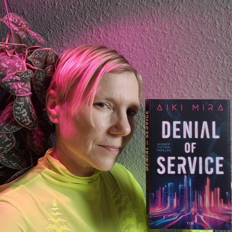 Aiki holds their new novel Denial of Service into the camera