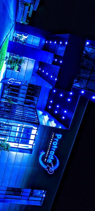 This photograph is an aerial view of a modern building complex at night, illuminated with blue lighting. The building is composed of multiple connected sections with flat roofs and large rectangular windows. Small trees are planted around the perimeter and within courtyards formed by the building structures. There are illuminated walkways and what appear to be small seating areas visible between the building sections. Along the lower right edge of the image, vertically oriented blue text reads "Protrade" with smaller text below reading "INTERNATIONAL BV". The overall image has a cool, monochromatic blue tone, creating a futuristic aesthetic.

Provided by @altbot, generated privately and locally using Gemma3:27b

🌱 Energy used: 0.108 Wh